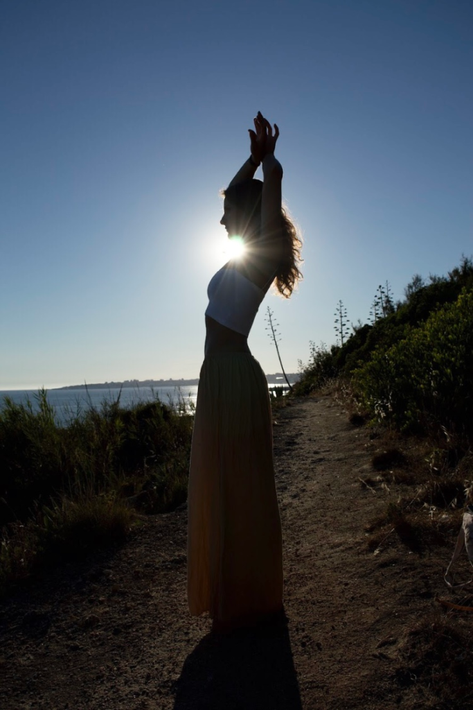 Natalie Montoya silhouetted against the sun on a coastal path above the sea