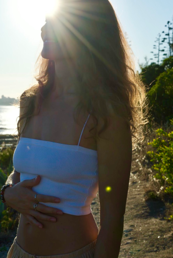 Natalie Montoya standing in the evening sun by the sea, hands resting on her belly